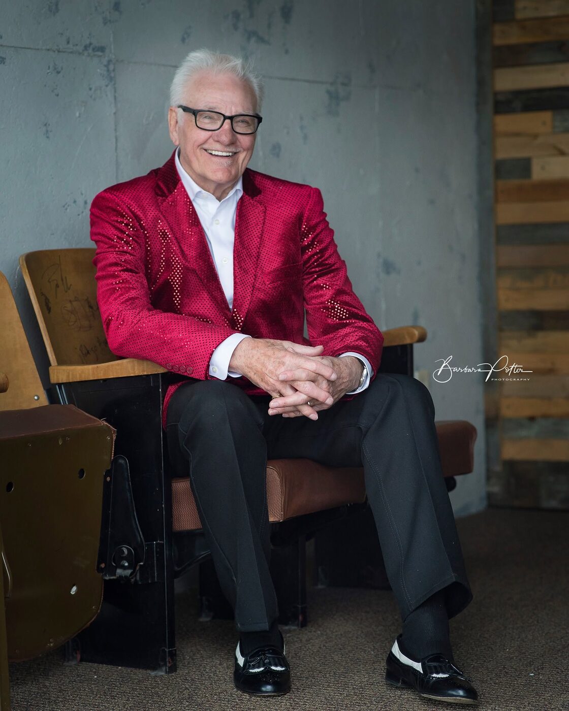 Jerry Foster in a red jacket, seated in a theater chair